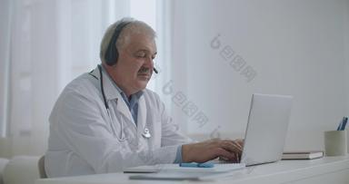 男性医生会说话的病人在线视频调用移动PC听耳机填充医疗报告工作远程